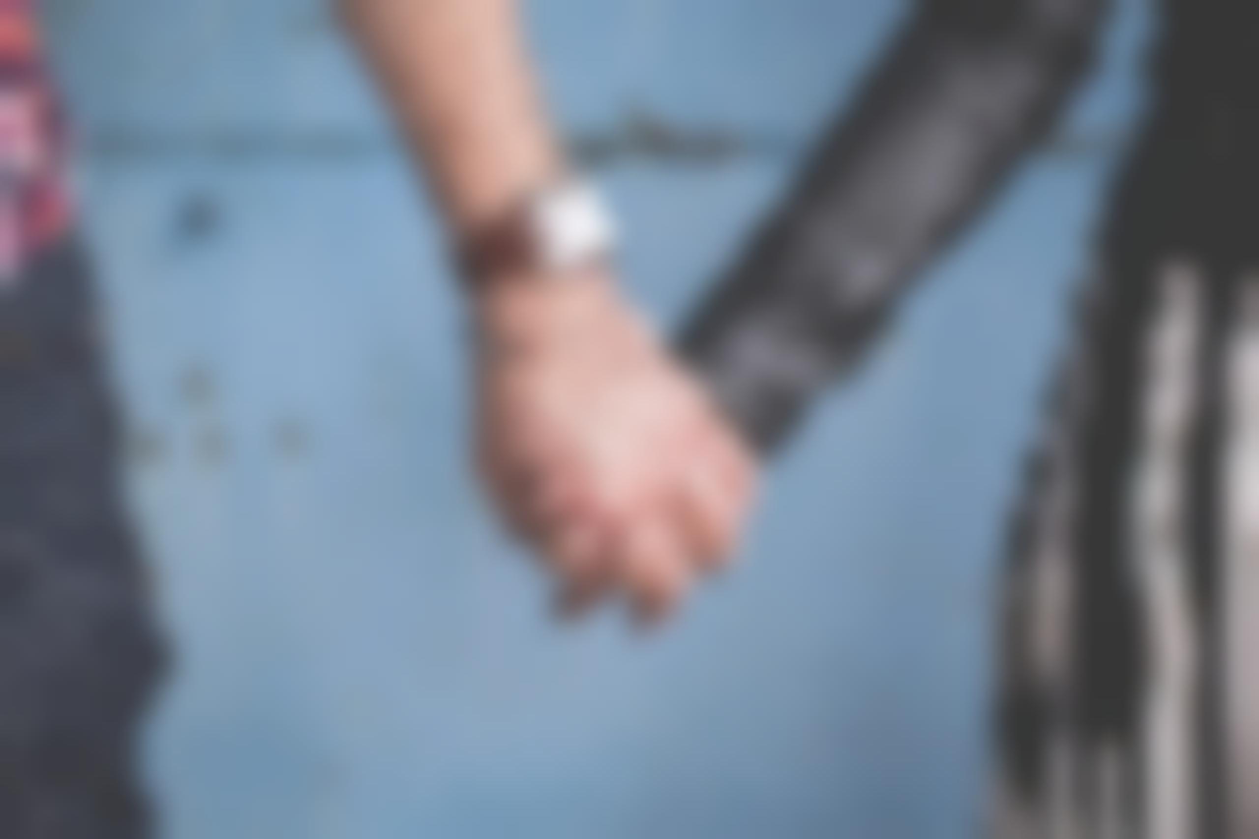 Couple holding hands in front of blue backdrop.