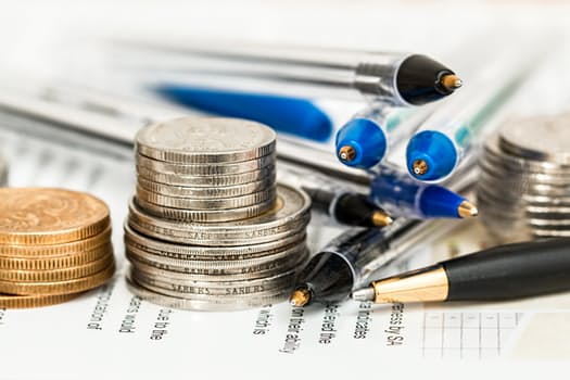 Various coins stacked next to pens on top of paperwork.