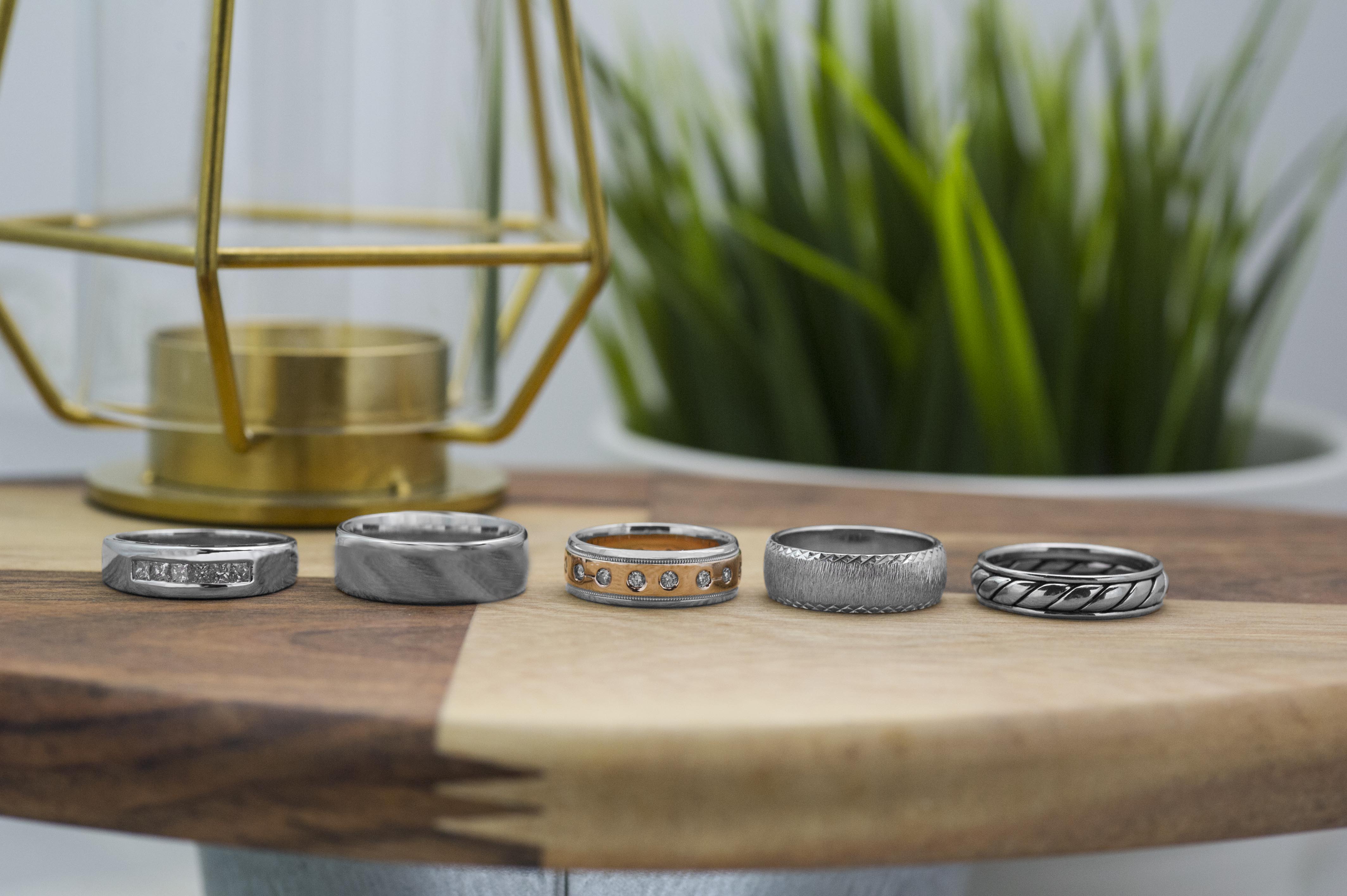 Five men’s wedding bands lined up on wooden table.