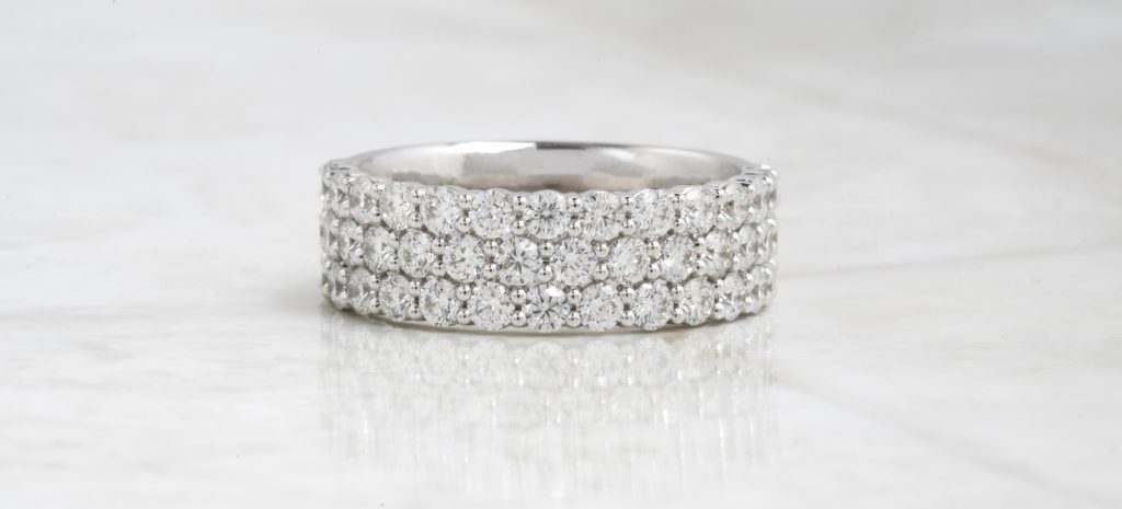 Three white gold stacking diamond eternity wedding bands on a white table.