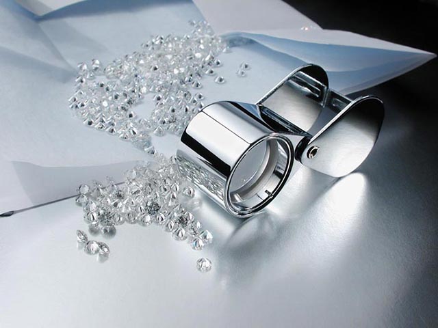 Loose cut diamonds on white table next to loupe.