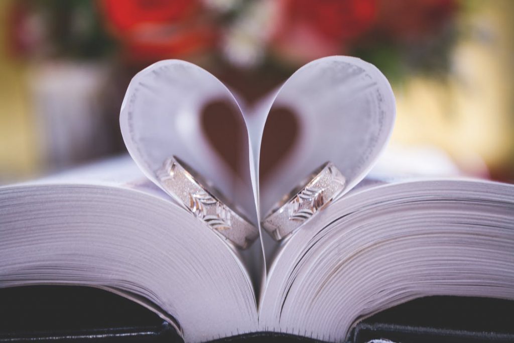 Two mixed metal wedding bands in-between heart-shaped pages of a book.