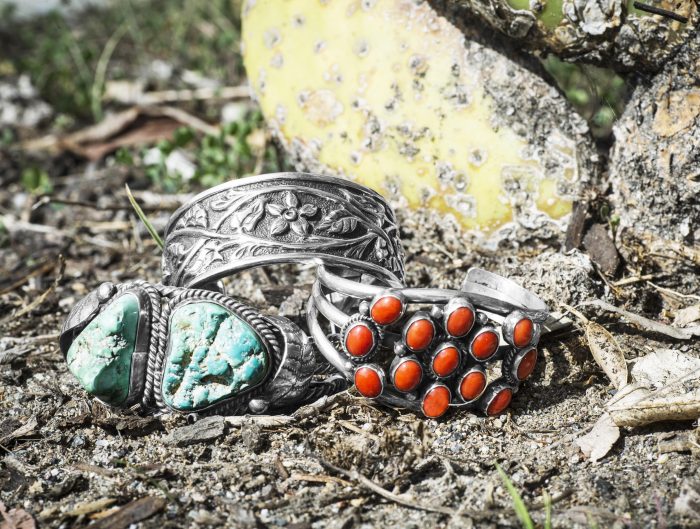 Three stacked sterling silver Native American cuff bracelets in outdoor scenery.