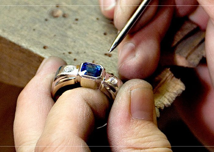 Jeweler setting a center stone into a ring at their bench.