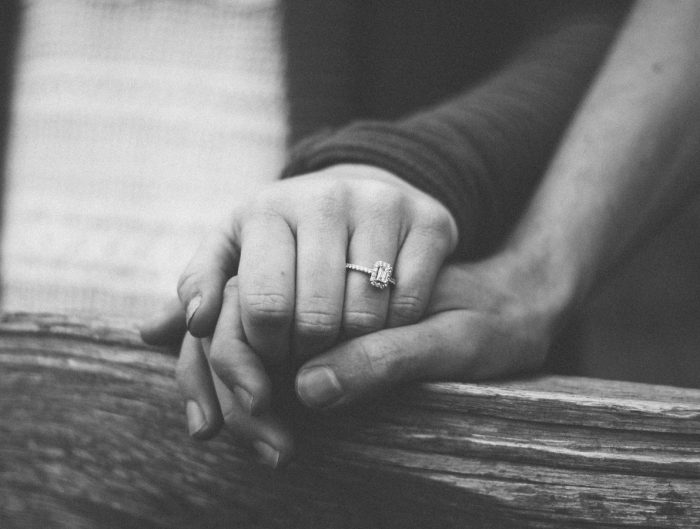 Black and white image of couple holding hands featuring diamond engagement ring.