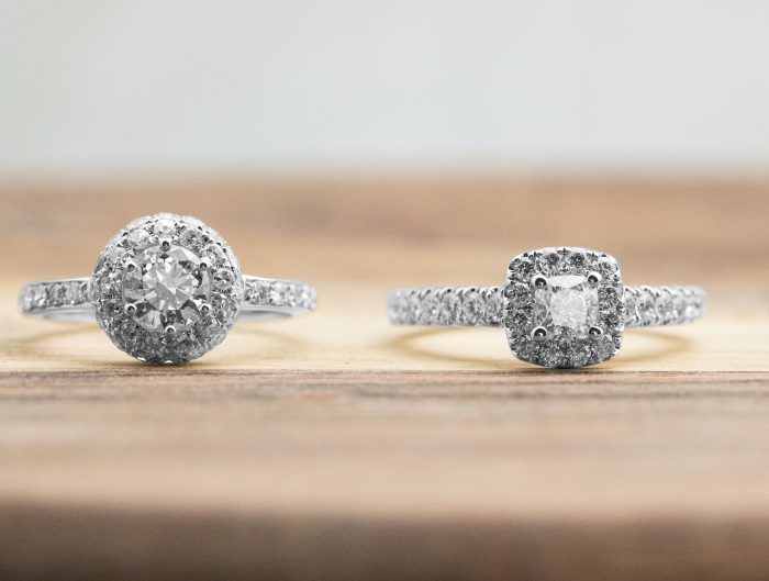 Four diamond engagement rings with diamond haloes on a wooden table.