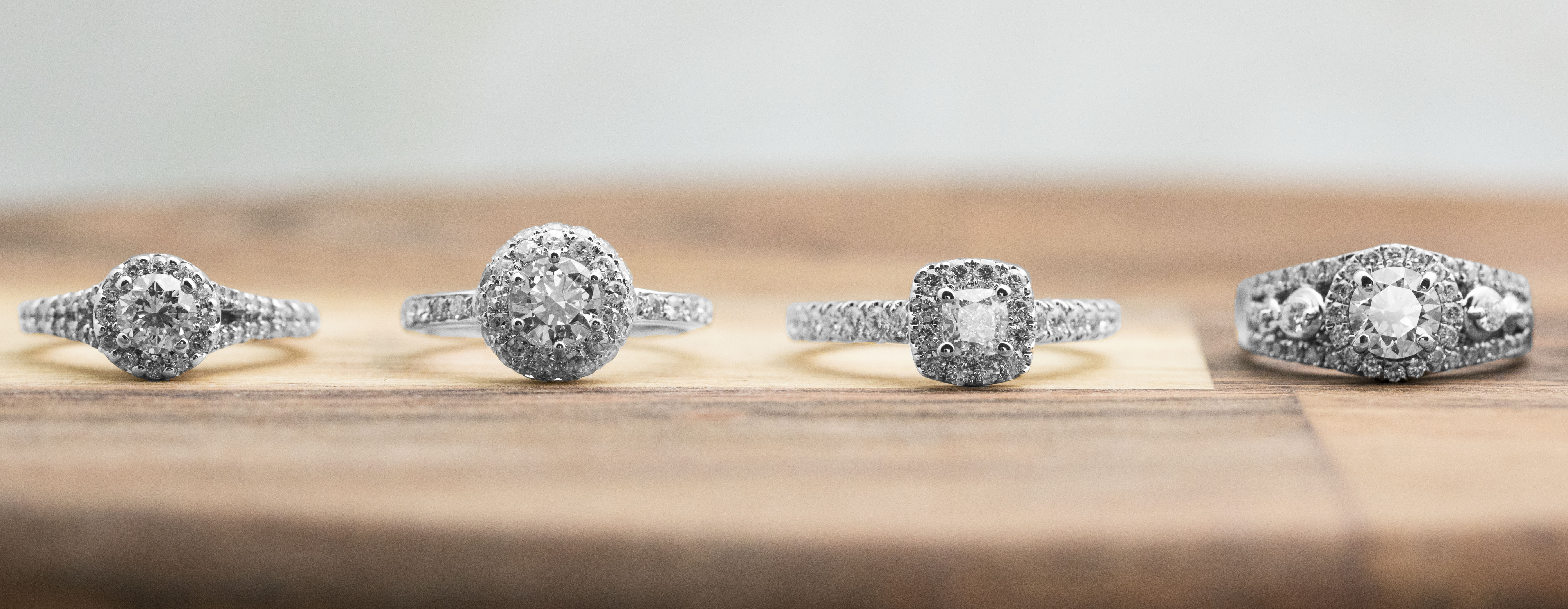 Four diamond engagement rings with diamond haloes on a wooden table.