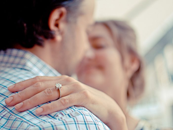 Woman’s hand on man’s shoulder featuring her diamond engagement ring.