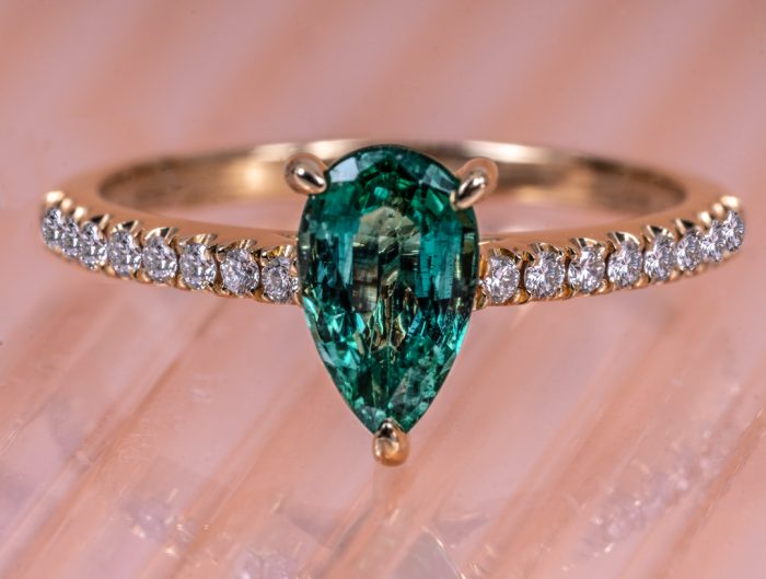 Yellow gold engagement ring centered with a pear cut emerald and diamonds in the band.