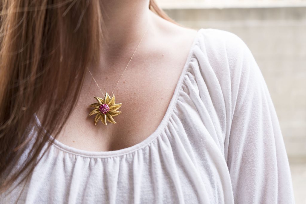 Woman wearing a yellow gold floral brooch as a pendant.