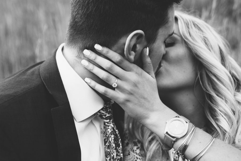 Married couple kissing and showing off woman’s hand with diamond engagement ring.