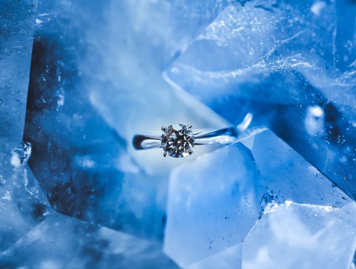 White gold solitaire engagement ring centered with a diamond on a blue ice background.