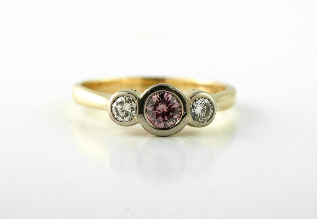 Yellow gold three-stone engagement ring centered with a light red gemstone and diamonds.