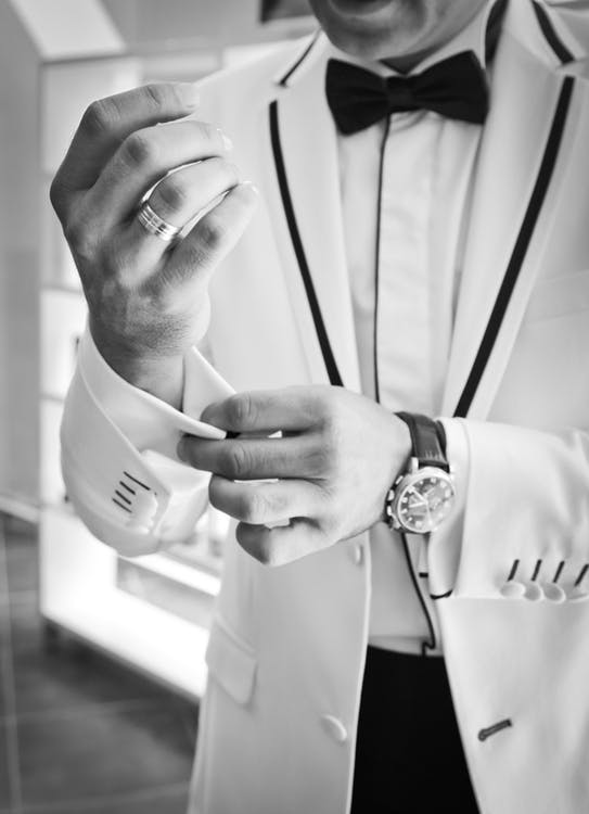 Groom wearing wedding band buttoning suits buttons at his wrist.