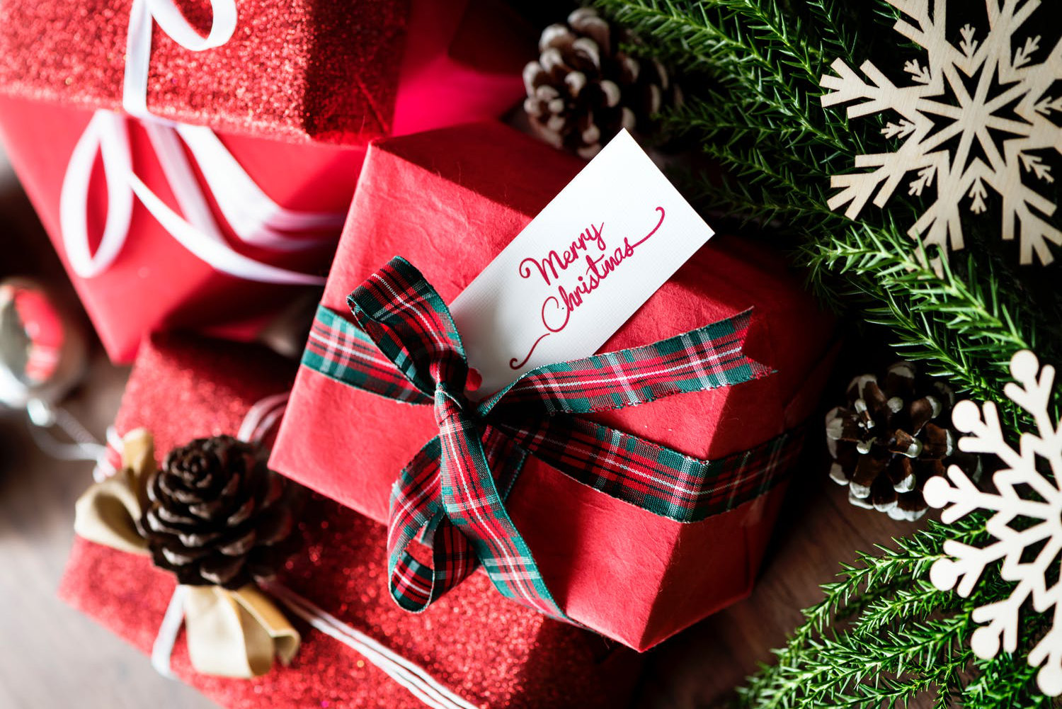 Gifts wrapped in red paper with Christmas ribbon and tag with text “Merry Christmas”.