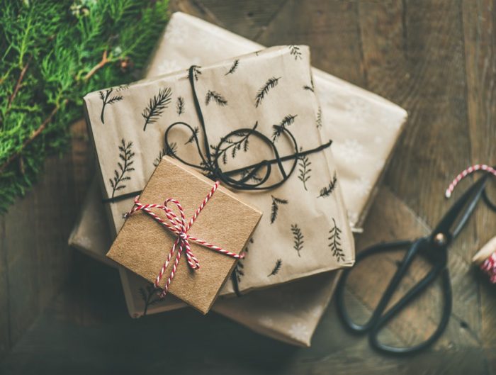 Three gift boxes wrapped in paper and twine stacked on a hardwood floor.