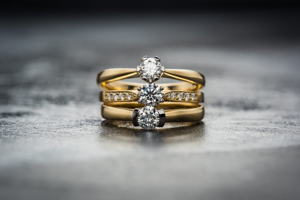 Three yellow gold engagement rings centered with diamonds stacked on a grey table.