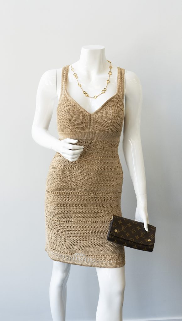 Mannequin with tan sleeveless dress, gold necklace, and vintage clutch wallet.