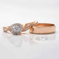 Rose gold twist diamond engagement ring with diamond halo and plain rose gold
wedding band on white table.