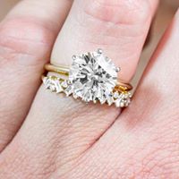 Woman wearing yellow gold solitaire diamond engagement ring and diamond eternity
band.