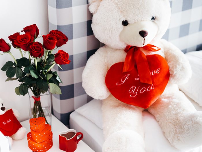 Valentine’s Day teddy bear and vase of red roses on nightstand.