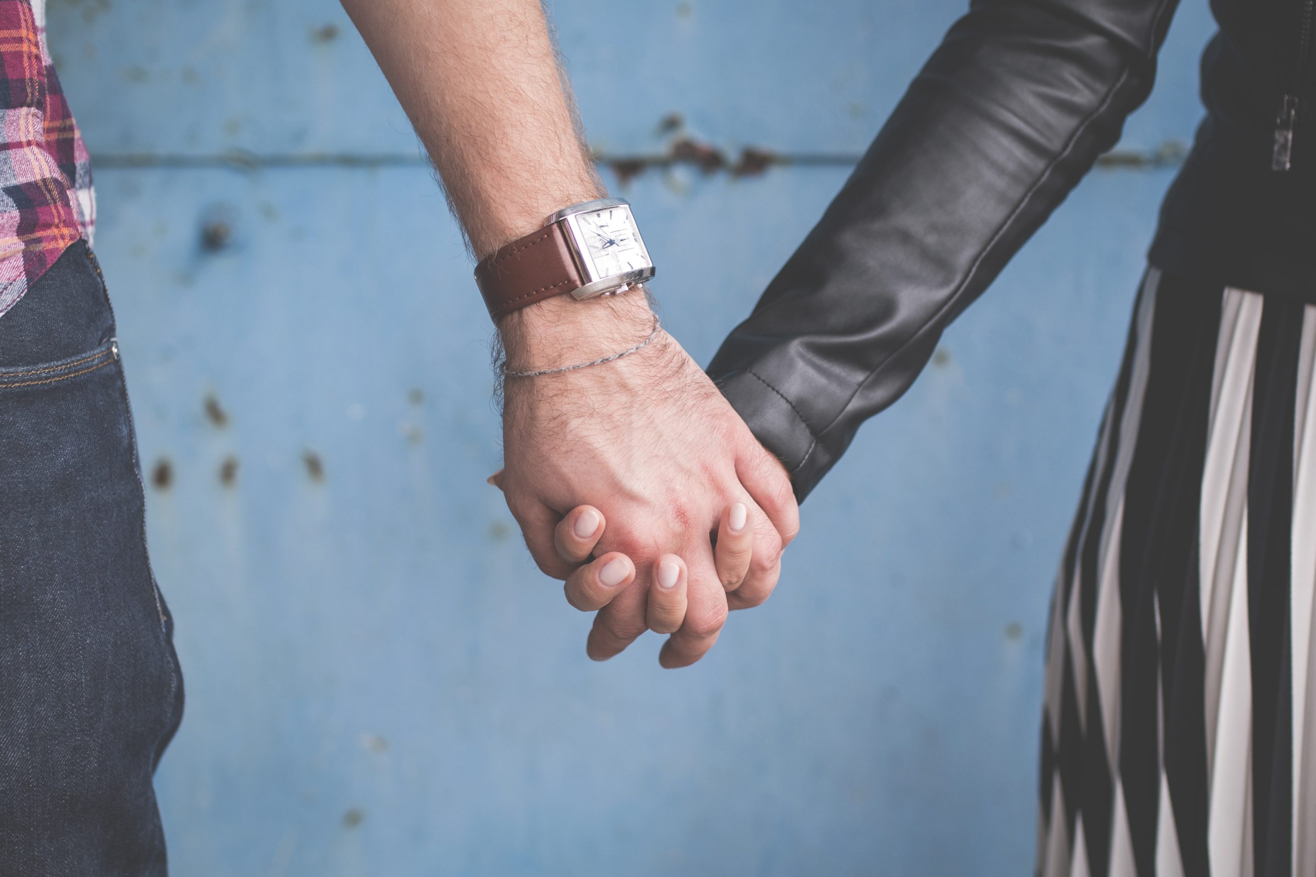 Couple holding hands in front of blue backdrop.