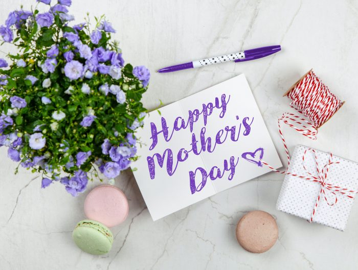 Mother’s Day card with two gift boxes and a vase of purple flowers on white table.