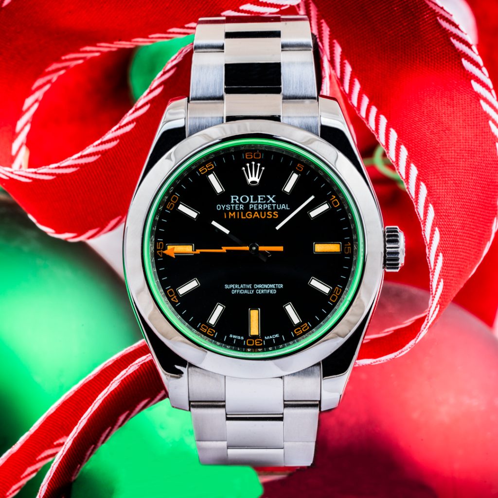 Pre-owned men’s Rolex Milgauss 40mm on a red ribbon background with green and red ornaments.