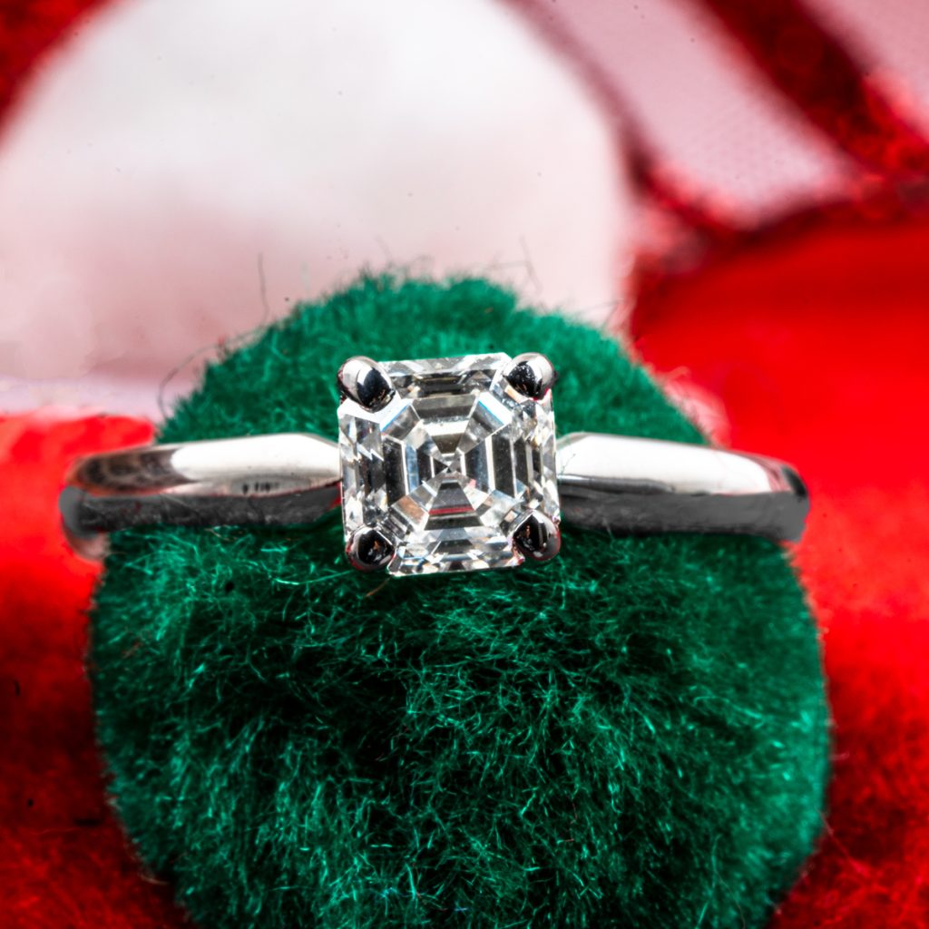 Vintage white gold solitaire diamond engagement ring displayed on a green pouf.