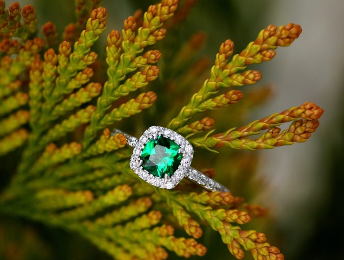 White gold engagement ring centered with a cushion cut emerald surrounded by a halo of round diamonds.