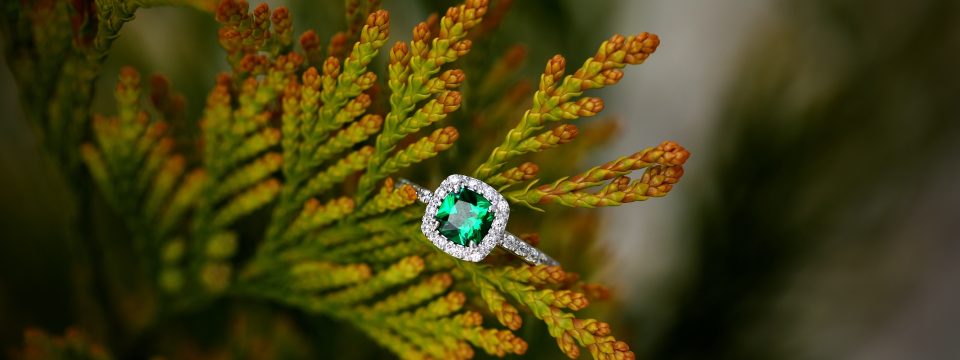 White gold engagement ring centered with a cushion cut emerald surrounded by a halo of round diamonds.