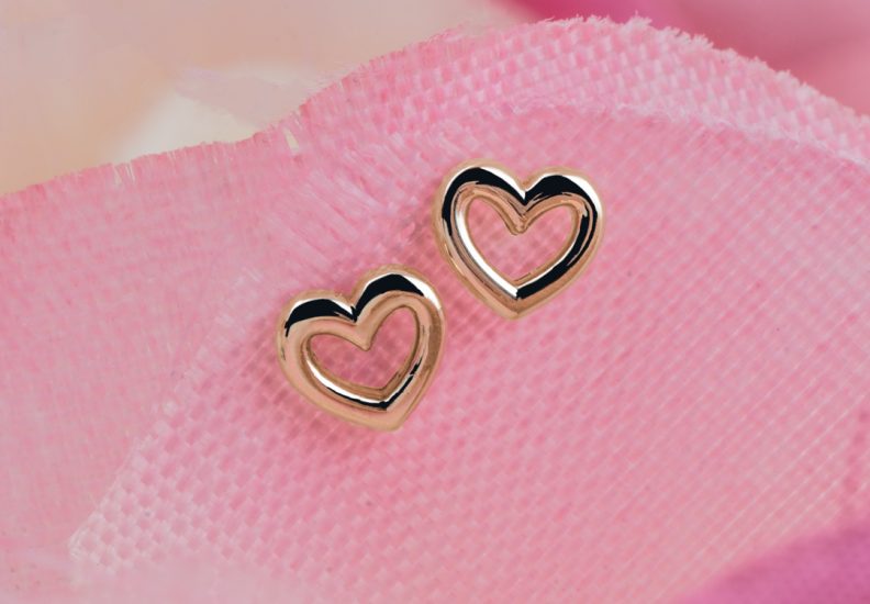 Yellow gold tiny hollow heart stud earrings on a pink flower petal.