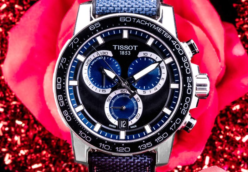 New men’s Tissot Supersport Chrono in stainless steel with a blue and black strap on a red rose background.