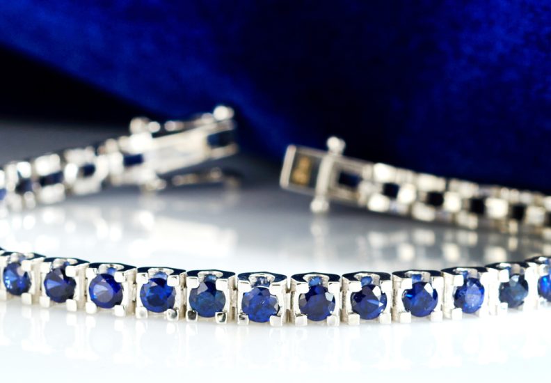 White gold diamond and blue sapphire tennis bracelet on a white table.