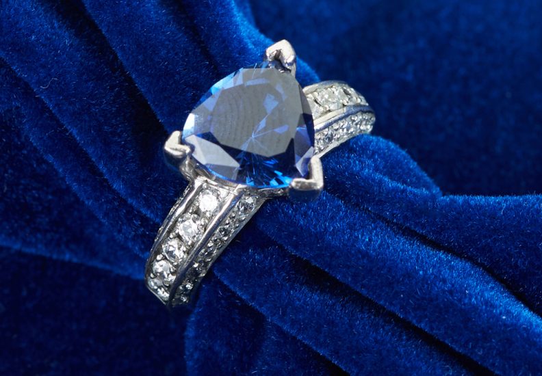 White gold engagement ring centered with a trillion cut blue sapphire and diamonds in the band.