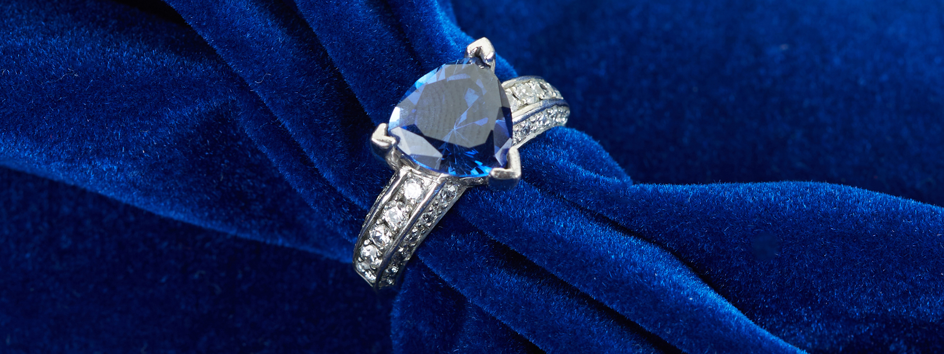 White gold engagement ring centered with a trillion cut blue sapphire and diamonds in the band.