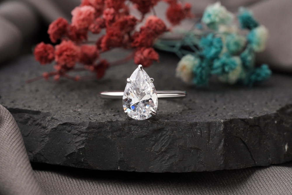 White gold solitaire engagement ring centered with a pear cut diamond on a stone background.