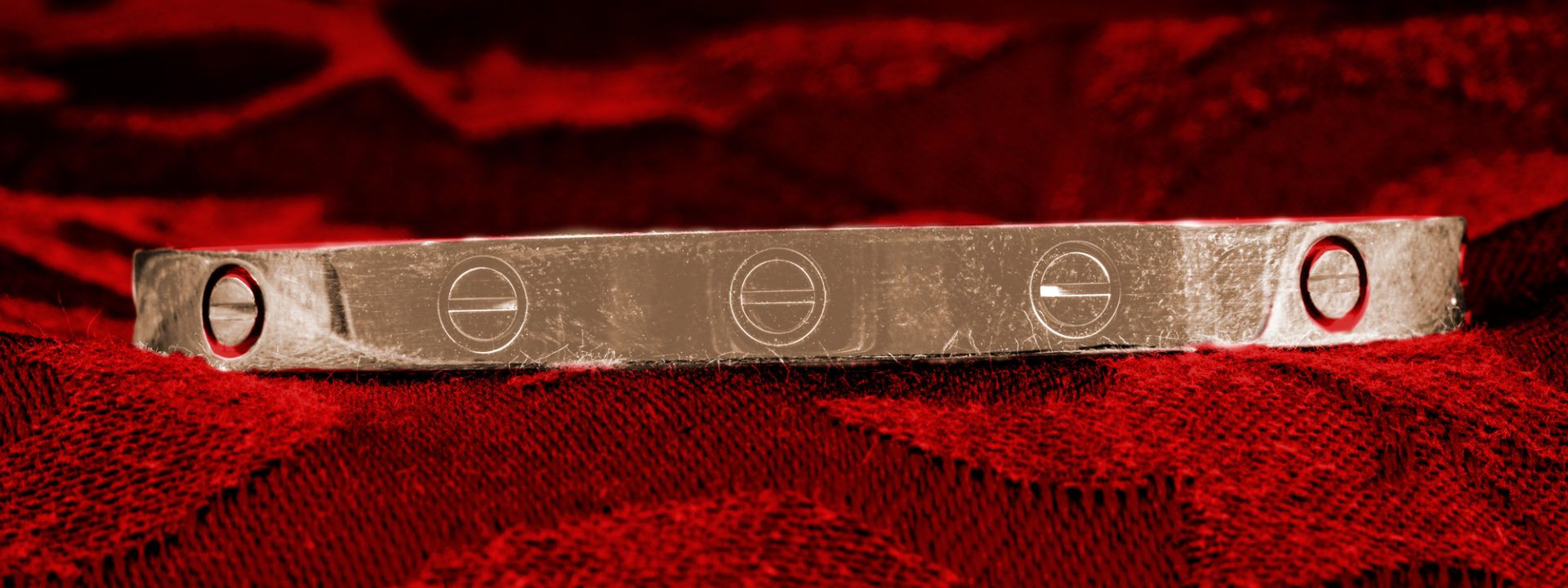 Vintage yellow gold Cartier LOVE bracelet on a red fabric background.