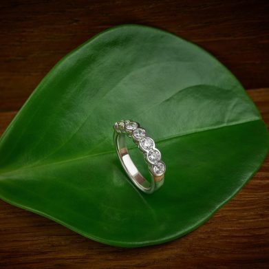 White gold and diamond bezel set wedding band sits on a green leaf