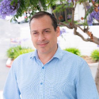 professional headshot of a man dressed in a light blue shirt with a blooming purple tree in the background