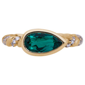 twisted gold ring featuring a pear shaped emerald and diamonds in the band on a white background