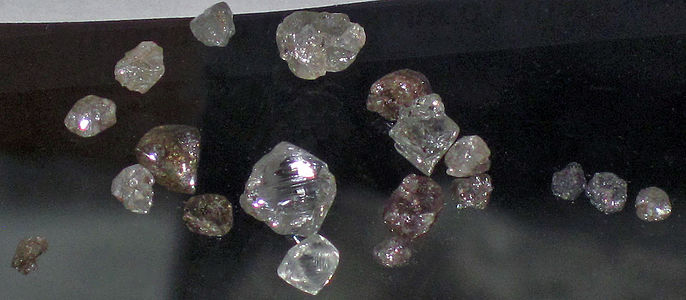 Rough uncut diamonds in various colors on black background.
