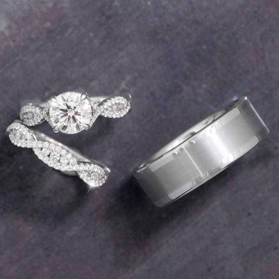 Diamond engagement and wedding ring set with an intricate twist design, paired with a sleek men's band on a dark background.