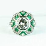 Antique platinum statement ring centered with a diamond surrounded by diamonds and emeralds.