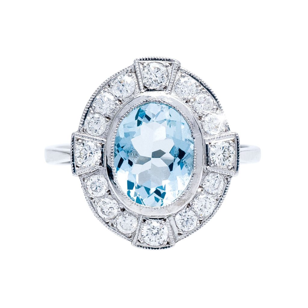 Oval-cut aquamarine ring with a diamond halo set in white gold, featuring an intricate vintage-inspired design.