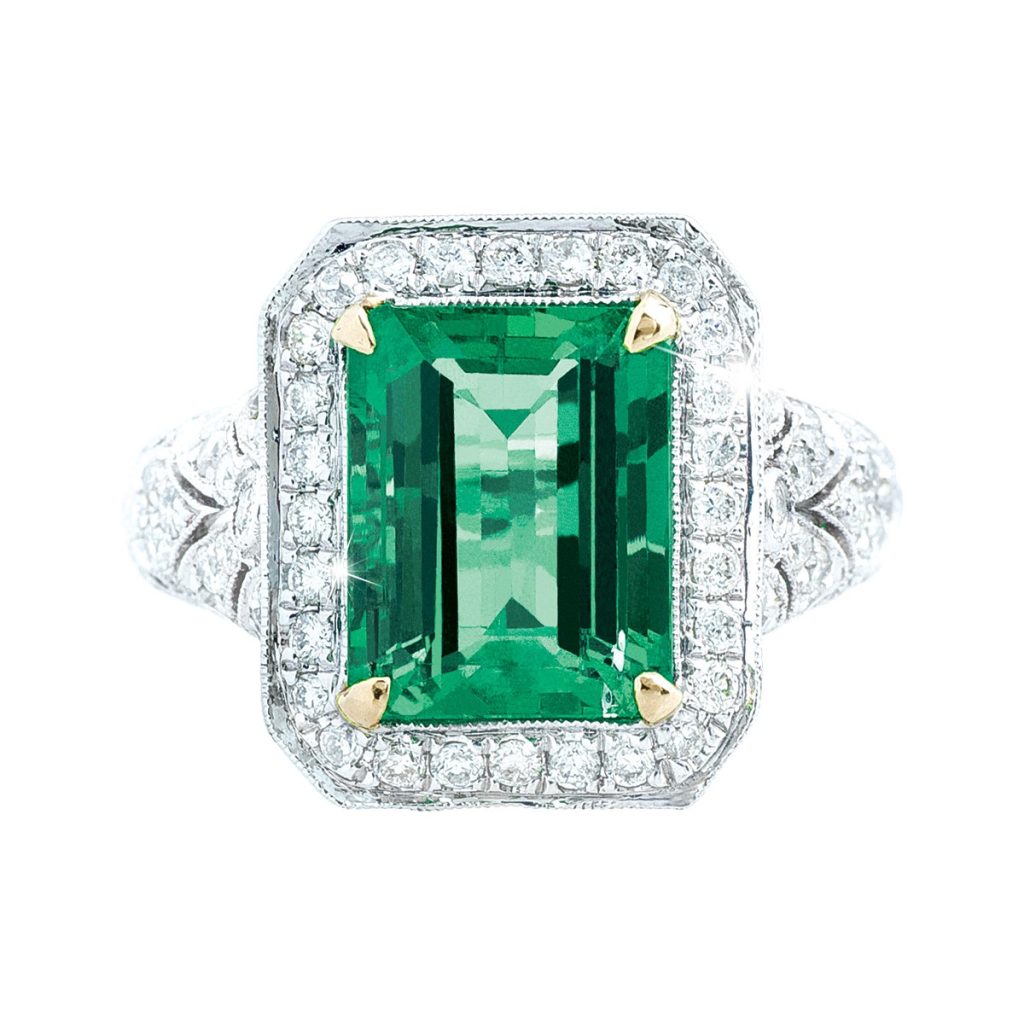 White gold engagement ring centered with an emerald surrounded by a diamond halo and
diamonds in the band.