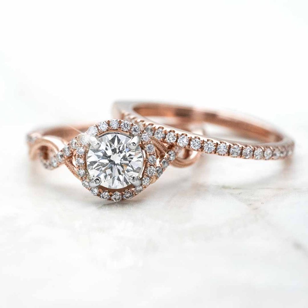 Rose gold diamond engagement ring with a round-cut center stone, halo setting, and a twisted pavé band, paired with a matching band.