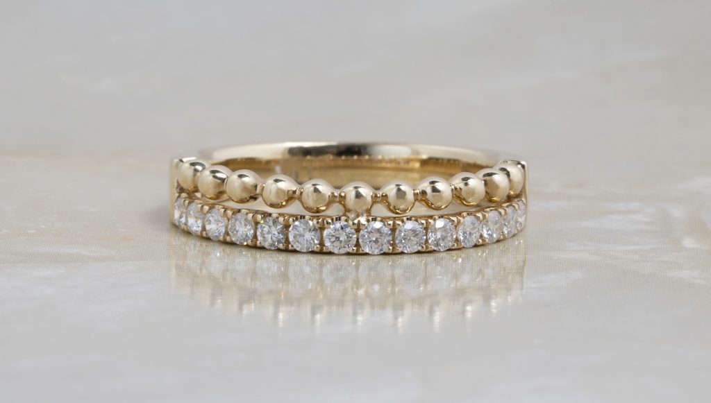 Two yellow gold wedding eternity bands, one with diamonds, stacked on a white table.