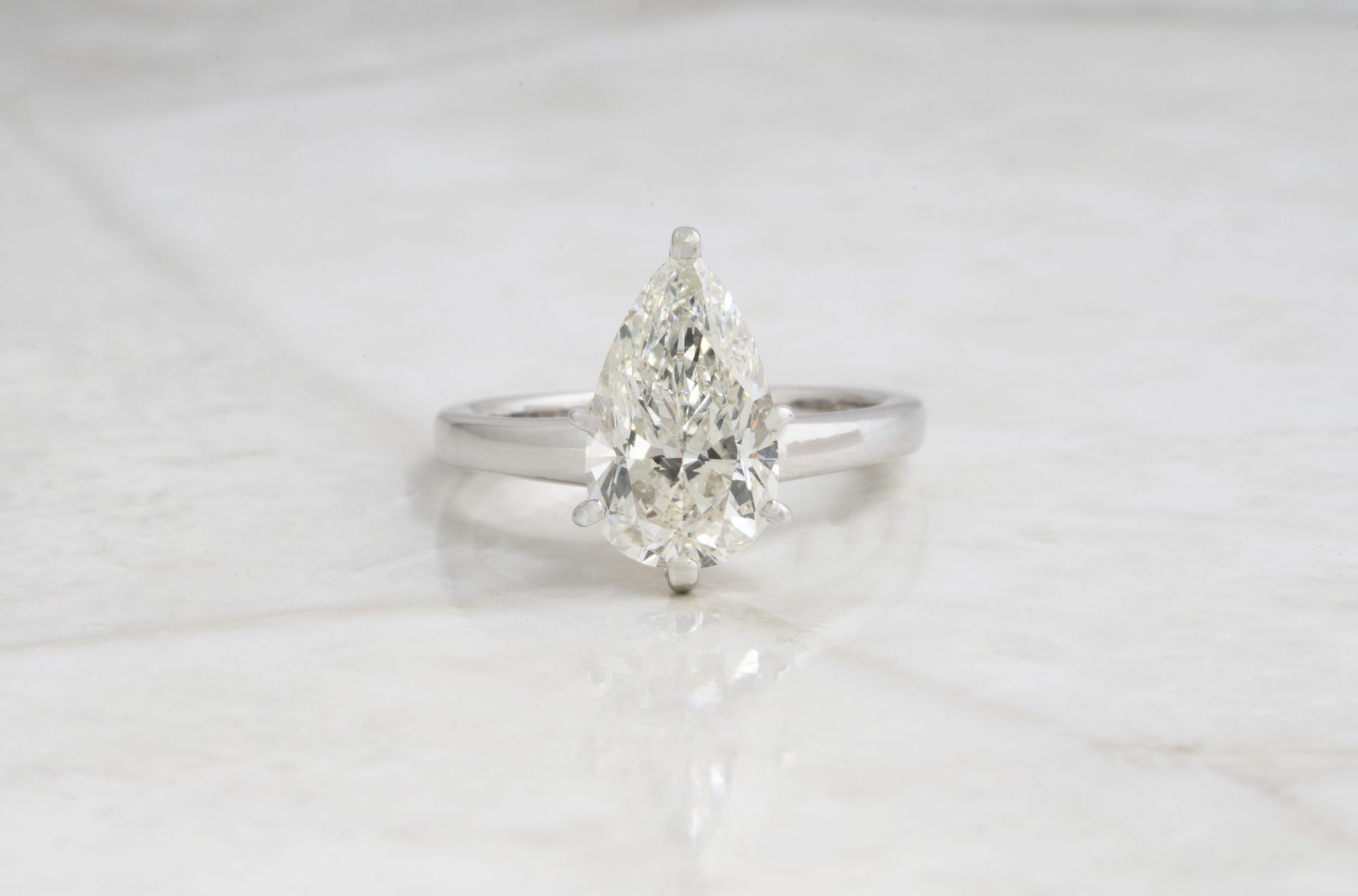 White gold solitaire engagement ring centered with a pear cut diamond.