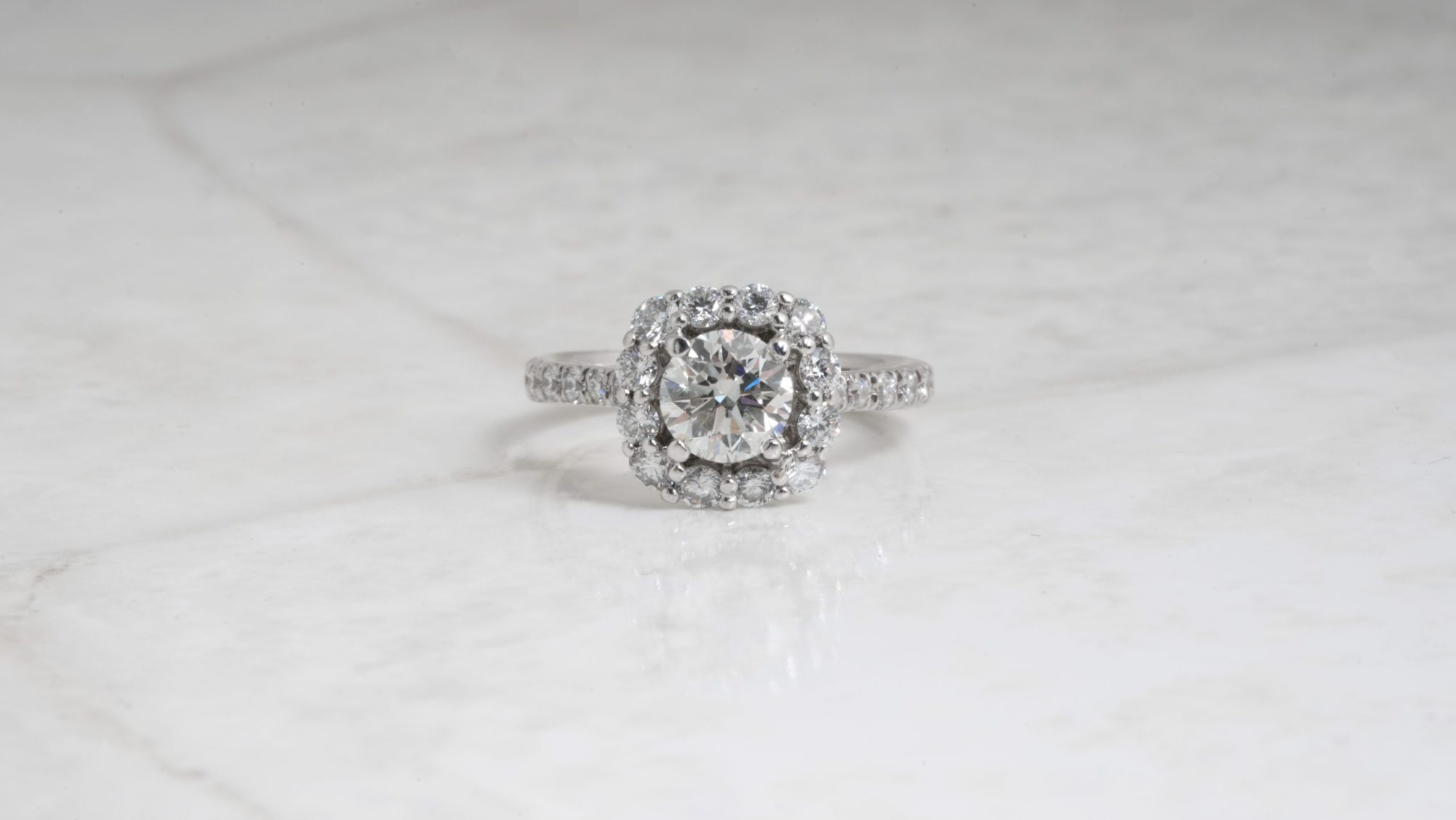 White gold engagement centered with a diamond surrounded by a diamond halo and diamonds in the band.